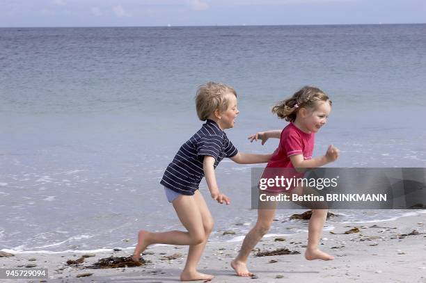 Un gar?on de 5 ans court apr?s une fille de 4 ans au bord de la mer.