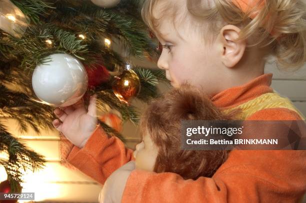 PETITE FILLE TOUCHE UNE BOULE DE NOEL.