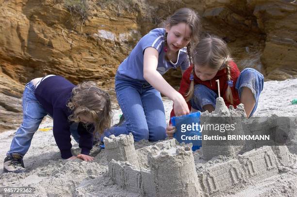 Trois filles construisent un ch?teau de sable sur la plage de l'Ile de Groix.