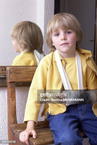 Un gar?on de 6 ans est assis sur un banc en bois portant un pl?tre ? l'avant-bras gauche.