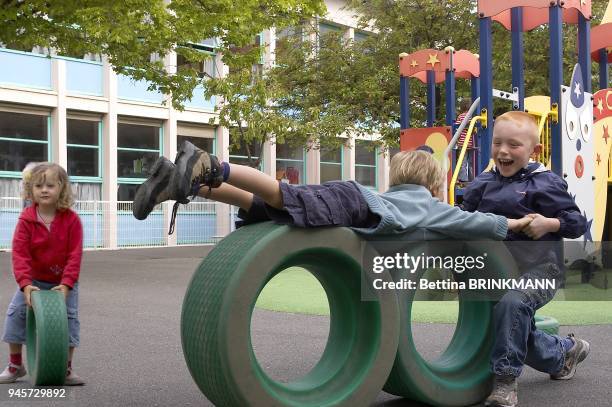 Deux gar?ons de 5 ans s'amuse dans la cour d'?cole ? se rouler sur des grandes roues tandis qu'une fille de 4 ans tient sa roue sagement.