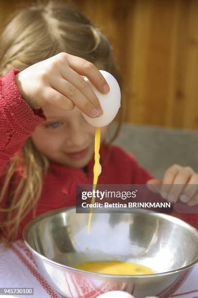 Une fille de six ans vide un oeuf et laisse couler le jaune dans un saladier. Une fille de six ans vide un oeuf et laisse couler le jaune dans un...