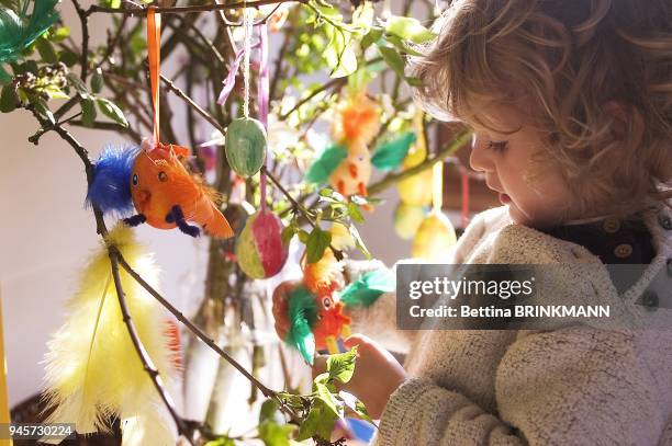 Une fille blonde au cheveux boucl?s de 3 ans contemple les d?corations accroch?es ? un bouquet de branches pour P?ques. Une fille blonde au cheveux...