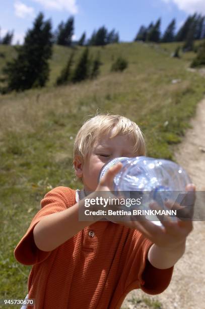 Un gacon de 5 ans boit de l'eau d'une bouteille lors d'une randonnee en montagne.