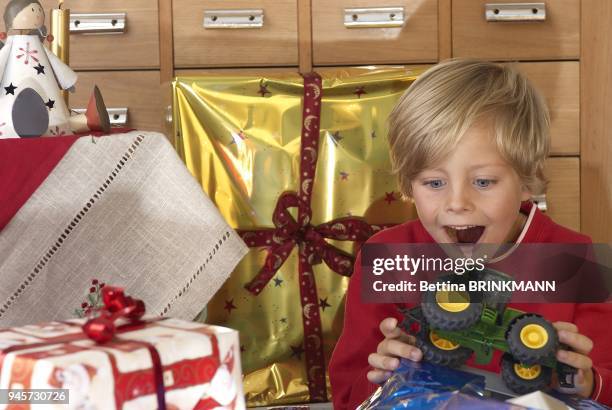 Un petit garcon de 6 ans deballe un tracteur comme cadeau de Noel et est tout content.