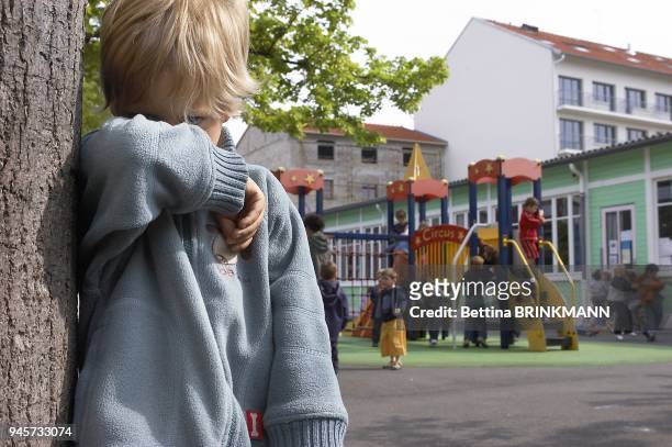 Un gar?on de 5 ans boude dans son coin dans la cour d'?cole pendant que les autres enfants s'amusent ensembles.