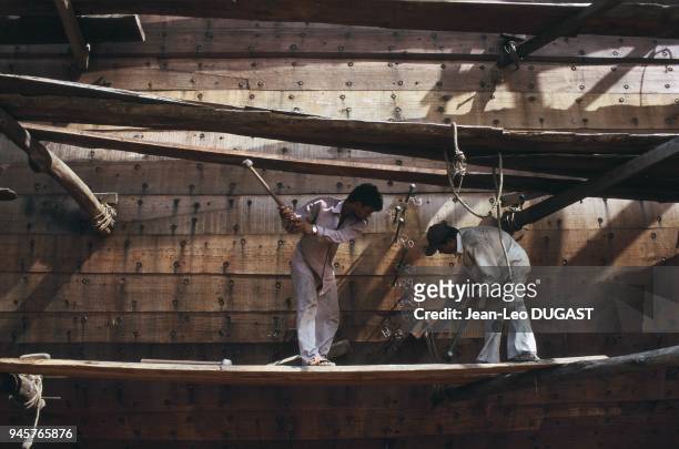 Workers nailing the hull noards of a cargo boat. Ouvriers clouant la coque du cargo.