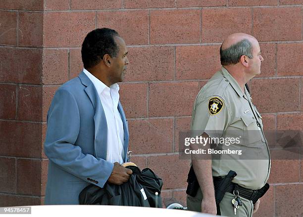 Simpson, the former football star, left, is escorted by a Las Vegas Metropolitan Police officer following his release from the Clark County Detention...