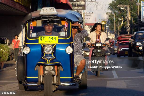 UN TUK TUK ET SON PASSAGER DANS LES RUES DE CHIANG MAI, THAILANDE.