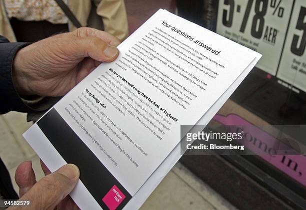 Northern Rock customers reads information handed out by the bank as they queue outside the branch in Golders Green, London, U.K., on Monday, Sept....