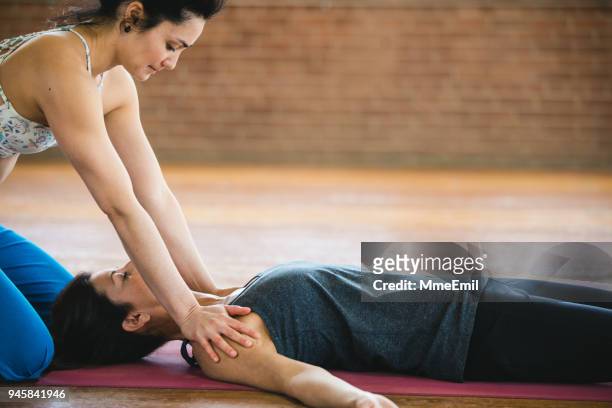 women practicing yoga position and massage. shavasana or corpse pose and shoulder massage - savasana stock pictures, royalty-free photos & images