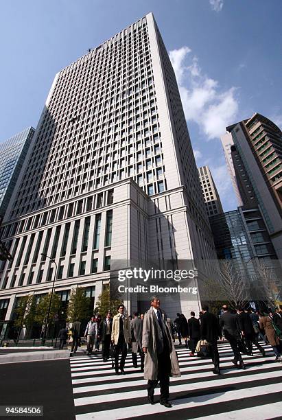 Pedestrians cross an intersection in front of the Hitachi Ltd. Headquarters in Tokyo, Japan, March 22, 2007. Hitachi Ltd., Japan's biggest...