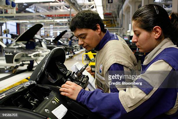 Maserati factory employee helps another assemble the dashboard of a Maserati Quattroporte automobile on the production line in the Maserati factory...