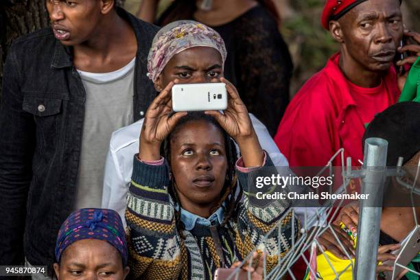 Young woman takes a photograph with her phone as the body of Winnie Mandela is returned to her home in Soweto the day before the funeral for the...