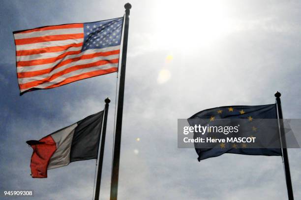 Les drapeaux am?ricain, Europ?en et Fran?ais, volent au vent ? contre jour sur fond de ciel bleu.