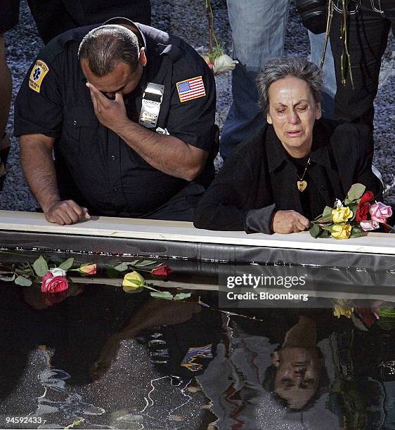 An unidentified Emergency Medical Technician and a woman weep as they kneel at a reflecting pool at the bottom of the Ground Zero, the former site of...