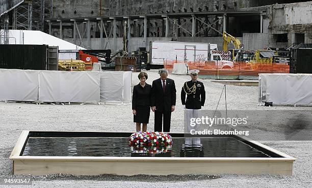 President George W. Bush, center, and first lady Laura Bush, left, flanked by a military officer, look on after laying a wreath during a memorial...
