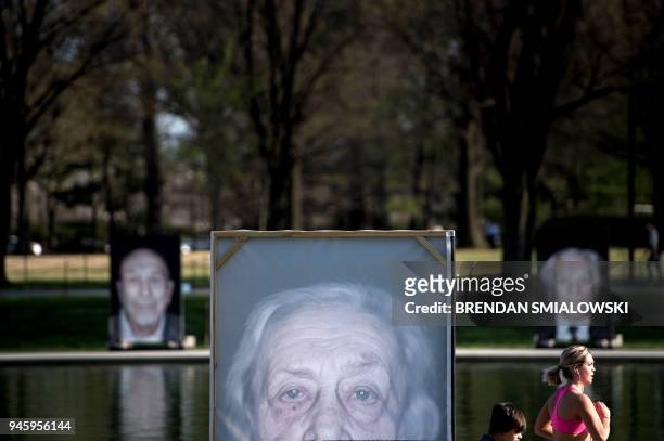 People pass portraits of Holocaust survivors during the Lest We Forget exhibition along the Reflecting Pool at the National Mall on Holocaust...