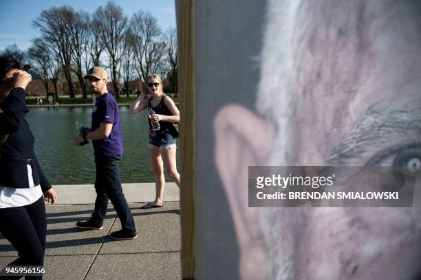 People pass portraits of Holocaust survivors during the Lest We Forget exhibition along the Reflecting Pool at the National Mall on Holocaust...