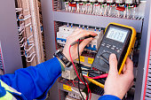 multimeter is in hands of engineer in electrical cabinet. Adjustment of automated control system for industrial equipment control cabinets. electrician measures voltage by tester.