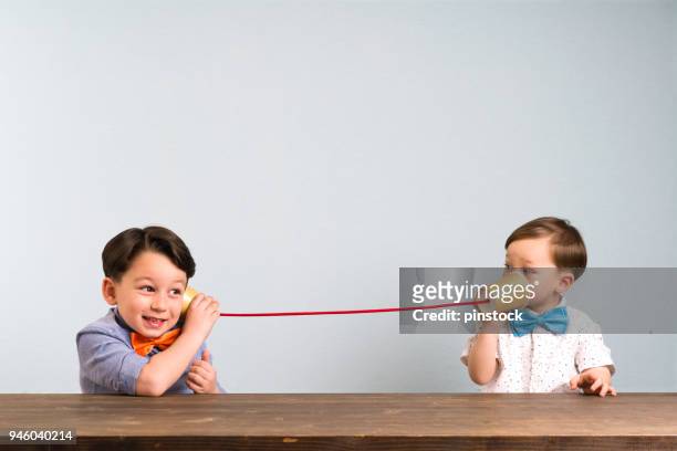 two childeren are using paper cups as a telephone - ear stock pictures, royalty-free photos & images