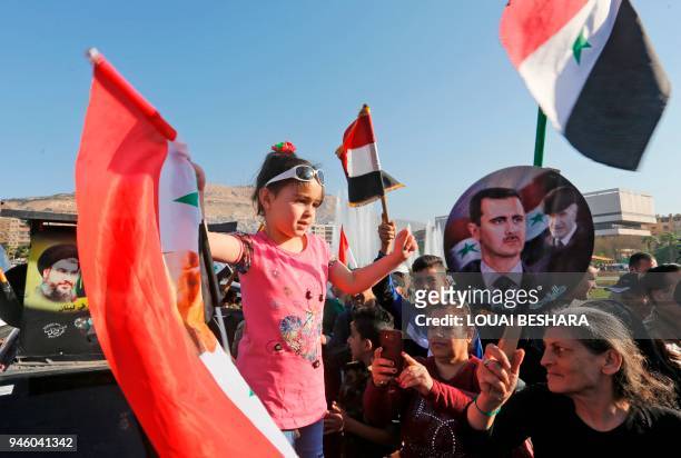 Syrians wave the national flag and portraits of President Bashar al-Assad as they gather at the Umayyad Square in Damascus on April 14 to condemn the...