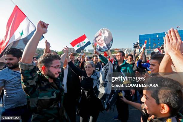 Syrians wave the national flag and wave portraits of President Bashar al-Assad as they gather at the Umayyad Square in Damascus on April 14 to...