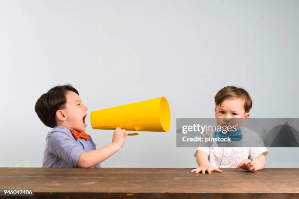 child is shouting through megaphone to another child - persuasão imagens e fotografias de stock