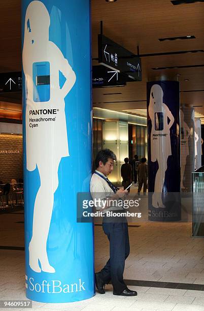 Man uses his mobile phone as he leans on a pillar covered in Softbank Corp. Advertising in Tokyo, Japan, on Monday, May 7, 2007. Softbank Corp.,...