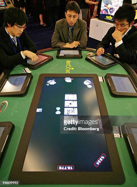 Visitors try out an electronic poker table which does not require playing cards, money or even a dealer to play at the third Asian Gaming Expo in...