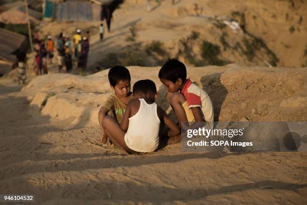 Three young children sit and play on mud steps in the hills of Kutupalong refugee camp. When Monsoon hits these steps will be a river of thick muddy...