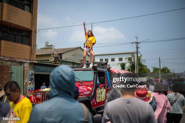 Pole dancer performs on the roof of a car as it joins the procession following the sedan chair carrying a statue of the goddess Mazu as it is carried...