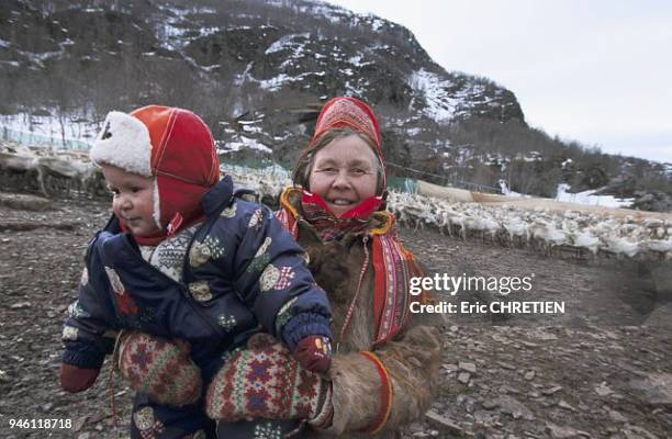 BIRIL LOGJE, FEMME SAMI REVETUE DE SON MANTEAU EN PEAU DE RENNE TENANT DANS SES BRAS SON PETIT-FILS, REGION DE KAUTOKEINO, LAPONIE, NORVEGE.