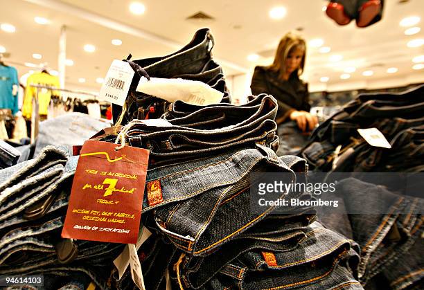 Stack of '7 for all mankind' jeans sit on display as a woman browses nearby inside the flagship Saks Fifth Avenue store in New York, Monday, March 5,...