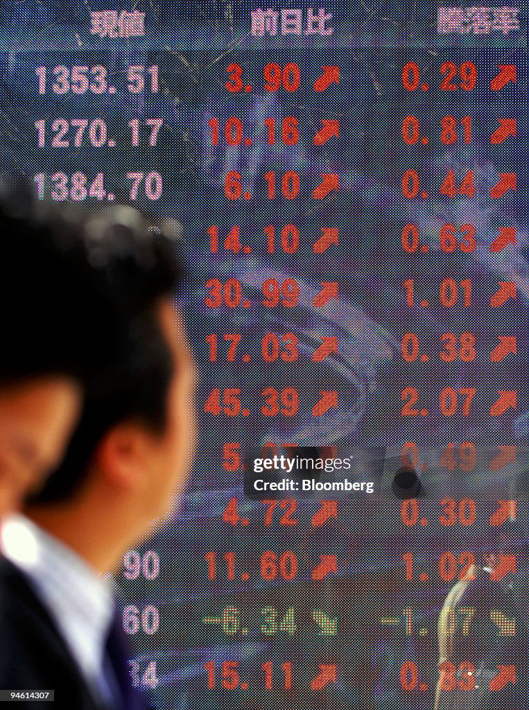 Pedestrians walk past an electronic stocks board showing ris
