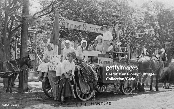 Black and white photograph showing men and boys, some dressed in women's Edwardian clothing, seated and standing on a horse-drawn, anti-suffrage...