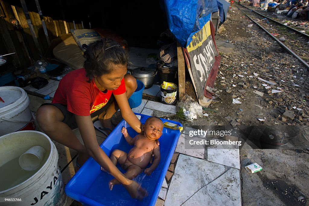 A Javanese migrant slum dweller washes her baby in her home