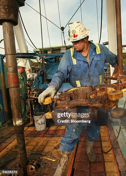 Worker Jay Banach, a "floor hand", wields the "tongs" in preparation of adding an additional 45 meter section of drill pipe, on a 4000-meter triple...