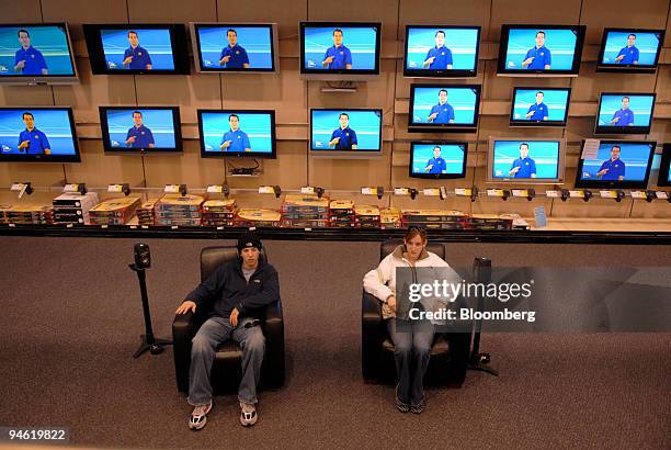 While a display of flat screen televisions play in the background, Marc Wells and Jessica Hohn watch a TV configured with surround sound inside a...