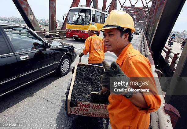 Highway maintenance workers wait for passing cars before moving on to fill holes in the road in Hanoi, Vietnam on Sunday, August 20, 2006.