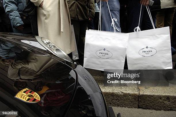 Shoppers with bags in front of a Porsche automobile wait for the Prada store on via Montenapoleone to open in Milan, Italy, Sunday, January 7, 2007.