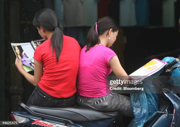 Women share the seat of a motorbike as theyt read magazines in Hanoi, Vietnam on Sunday, August 20, 2006.