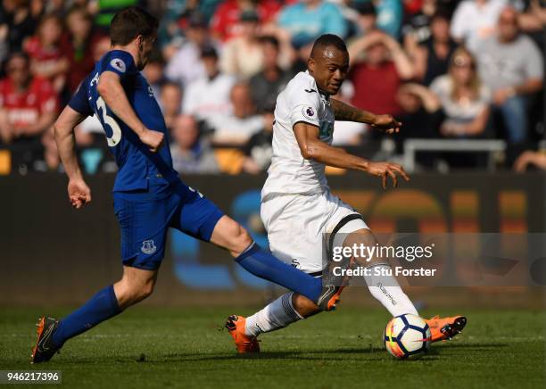 Swansea player Jordan Ayew shoots at goal despite the challenge of Phil Jagielka during the Premier League match between Swansea City and Everton at...