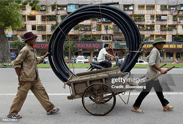 Workers push a trolly loaded with plastic piping along a street in Hanoi, Vietnam on Saturday August 19, 2006.