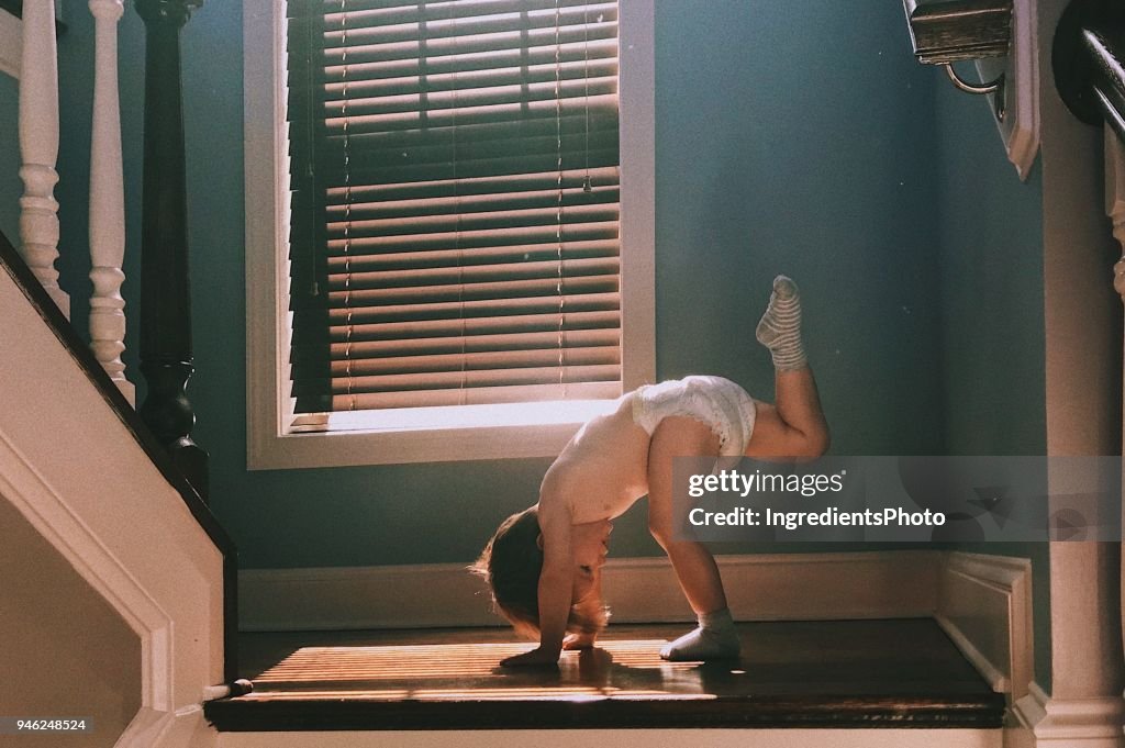Two years old toddler wearing diapers doing Yoga on the stairs at home