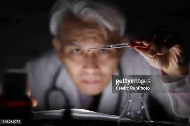 middle aged doctor dropping liquid with pipette - scientist in laboratory stockfoto's en -beelden