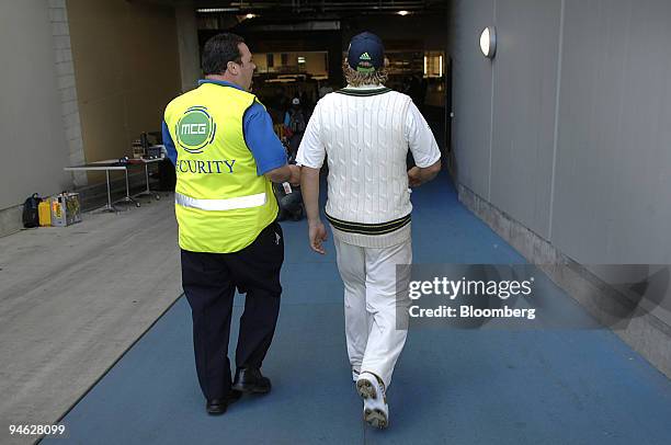 Shane Warne, of Australia, walks down the payers race with a secuity guard at the Melbourne Cricket Ground, after Australia won the fourth Ashes...