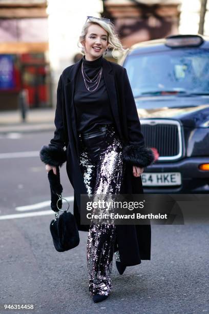 Guest wears a black turtleneck top, a balck coat, a black bag, silver glitter pants, during London Fashion Week February 2018 on February 16, 2018 in...