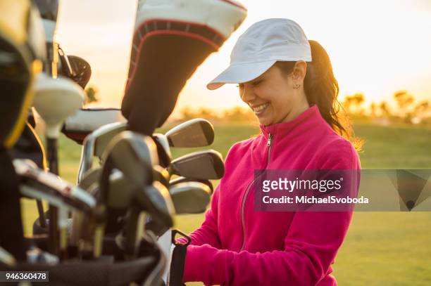female golfer grabbing clubs out of her golf bag at sunset. - golf stock pictures, royalty-free photos & images