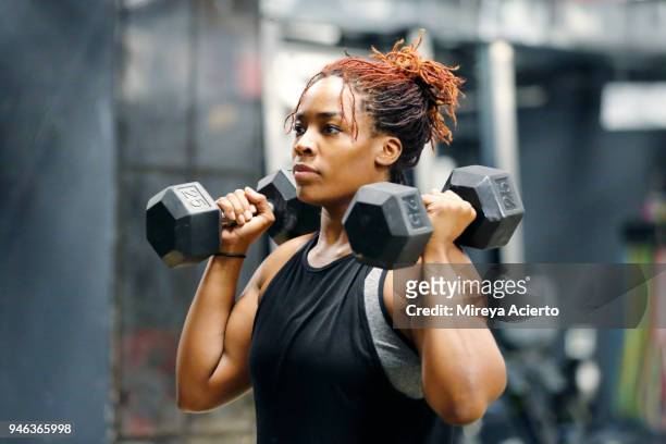fit, young african american woman working out with hand weights in a fitness gym. - sollevamento pesi foto e immagini stock